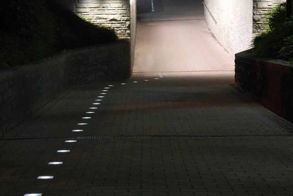 Fußweg zu einer Unterführung bei Nacht, leuchtende Steine führen am Wegrand entlang
