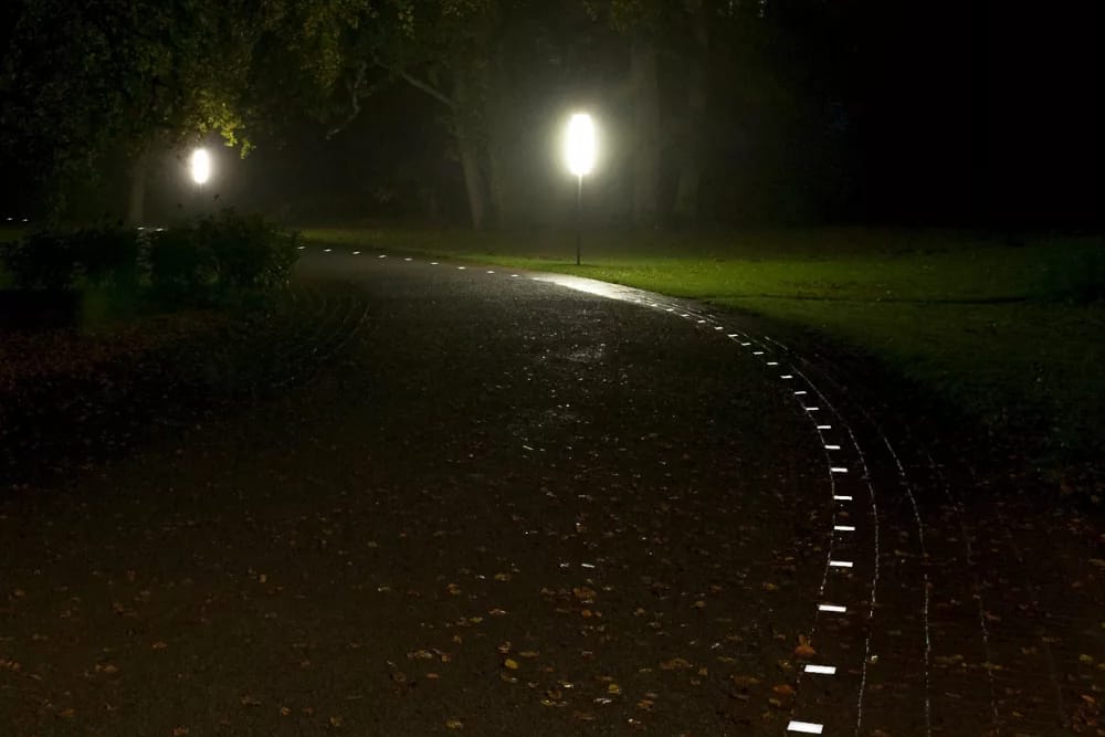Geschwungener Weg durch eine Grünanlage bei Nacht, leuchtende Steine folgen der Wegkante