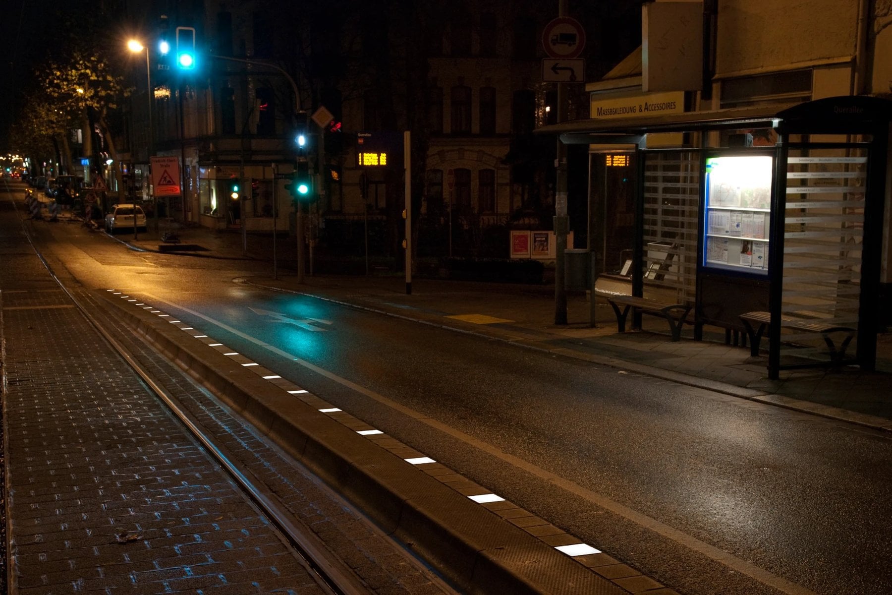 Haltestelle an einer Straßenbahnstrecke bei Nacht, leuchtende Steine markieren die Bordkante