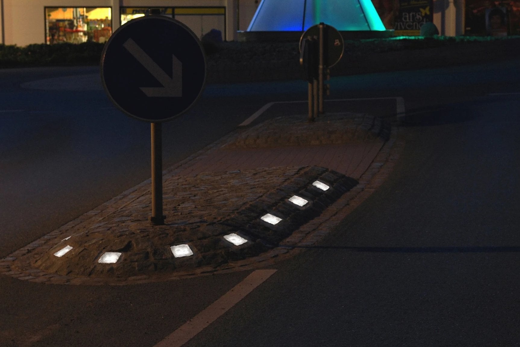 Verkehrsinsel bei Nacht mit Richtungsschild, leuchtende Steine an der Inselspitze